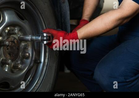 Automotive engineer operating hand tools on car in repair centre, while replacing wheel and tires - Maintenance technician servicing truck during routine vehicle service inspection Stock Photo