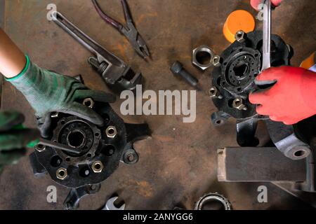 Overhead view of mechanical engineers working together as a team, repairing and overhauling car auto parts on a workshop bench using metal hand tools, while wearing protective workwear Stock Photo