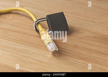Closeup shot fo a lock around a yellow LAN cable on a wooden surface Stock Photo