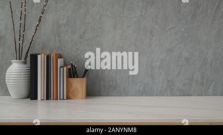 Close up of trendy workspace with books, stationery and ceramic vase on marble desk with grey loft wall background Stock Photo