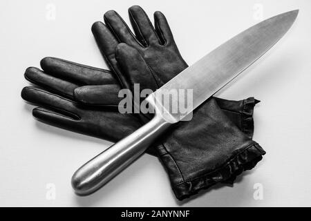 Overhead shot of a metal knife over black gloves on a  white surface Stock Photo