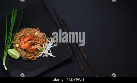 Top view of Pad Thai, stir fly of Thai noodle with shrimp and egg in black ceramic plate with copy space on black table Stock Photo