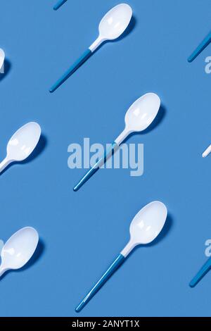 Pattern of white plastic spoons on blue background. Vertical picture. Flat lay, top view.