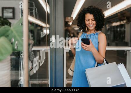Smiling young woman reading a cellphone text while out shopping Stock Photo