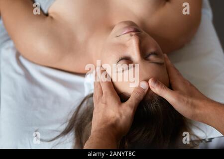 Young beautiful woman enjoying anti-aging facial massage.Male therapist making head massage to female client.Professional masseur.Relaxation,beauty Stock Photo