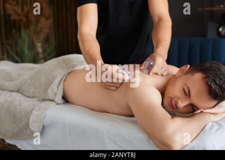 Cupping massage. Young man enjoying back and shouders massage in spa.Professional massage therapist is treating a male patient.Relaxation,beauty,body Stock Photo