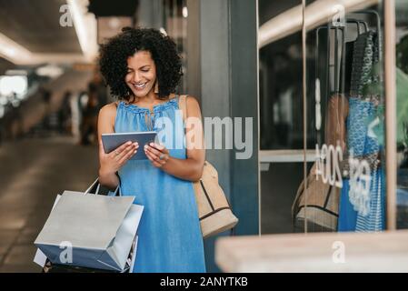 Young woman smiling and using a tablet while out shopping Stock Photo
