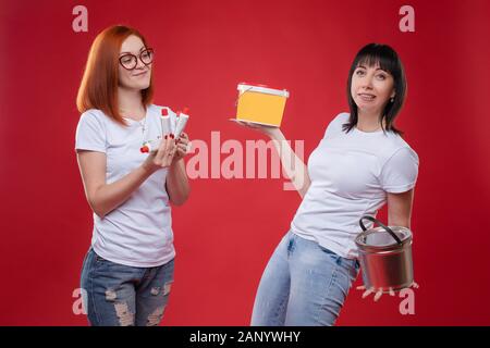Stock photo of red-haired girl in glasses with some glue tubes and dark-haired woman holding tubs of materials for constructing. Woman with tubs of bu Stock Photo