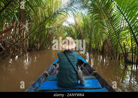 Boat tour in the Mekong River Delta region, Ben Tre, South Vietnam. Tourist with vietnamese hat on cruise in the water canals through coconut palm tre Stock Photo