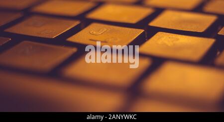 Black keyboard lit by orange light, macro photo. Stock Photo