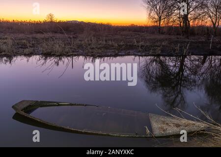 Typical wooden boat submerged in water in the wet area called Padule di Fucecchio, Tuscany, Italy, at sunset Stock Photo