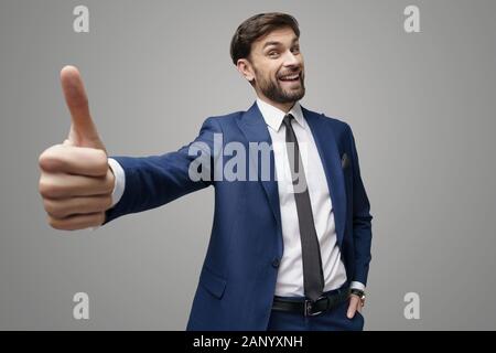 wide angle selfie shot of young business man going thumb up on grey background Stock Photo