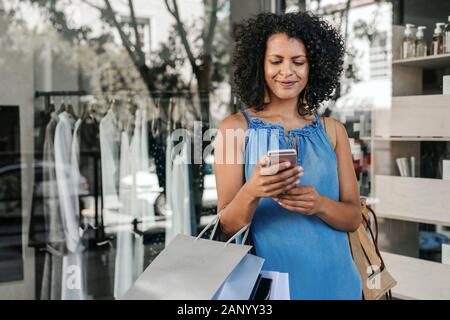 Smiling young woman reading a text message while out shopping Stock Photo
