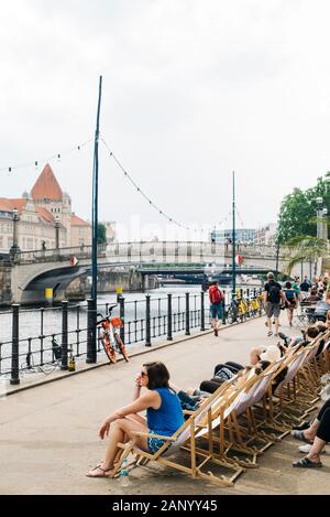 BERLIN, GERMANY - MAY 27, 2018: People relaxing sitting on deck chairs in the riverside of the Spree River, with the Monbijoubrucke bridge in the back Stock Photo