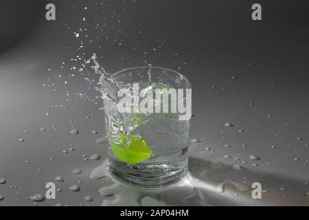 Colorful cubes dropped in a glass full of water, making beautiful splashes and wetting the table Stock Photo