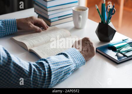 Close-up hands of the teacher man is preparing for the lesson: reading a book and making notes at the table, next to a pile of books and stationery, e Stock Photo