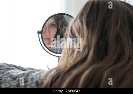 Depressed woman looks herself into mirror with sad face. Concept of mental illness in young woman Stock Photo