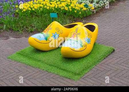 Typical yellow dutch wooden shoes clogs or klompen, painted with windmill and flowerbed behind, Netherlands Stock Photo