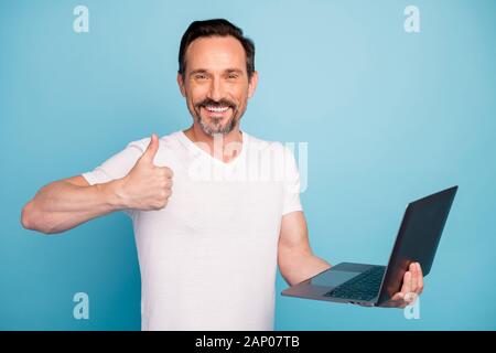 Close-up portrait of nice attractive cheerful cheery guy IT programmer geek holding in hands laptop showing thumbup isolated on bright vivid shine Stock Photo