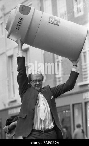 1980s, historical, In a street, a man holding up a large plastic litter bin. Started in 1954, when the National Federations of Women's Instutes passed a resolution to 'Keep Britain Tidy', in the 1980s, the environmental charity made a big impact with the message that to improve the urban environment, it was important that everyone tried to avoid litter. Stock Photo