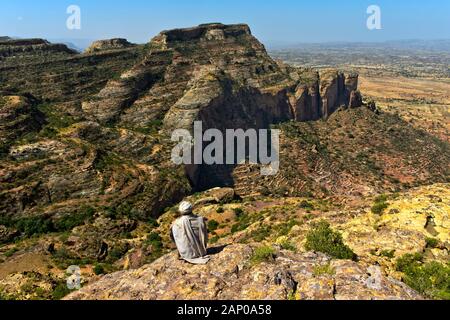 Local man sitting on a rock ledge and overlooking the rugged landscape of the Gheralta escarpment, near Hazwien, Tigray, Ethiopia Stock Photo