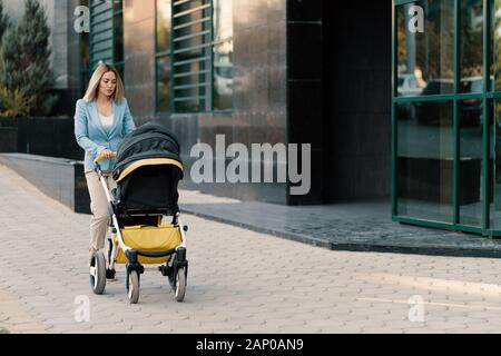 Portrait of a successful business woman in blue suit with baby. Business woman pushing baby stroller Stock Photo