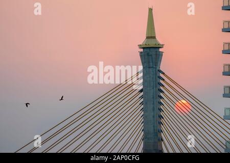 Closeup silhouette of a Bhumibol Bridge with the sun going down over the bridge during orange sunset sky.