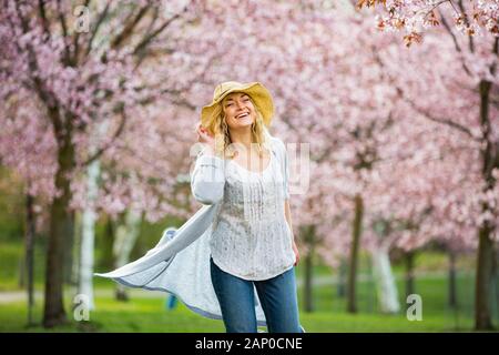 Young woman enjoying the nature in spring. Dancing, running and whirling in beautiful park with cherry trees in bloom. Happiness concept Stock Photo
