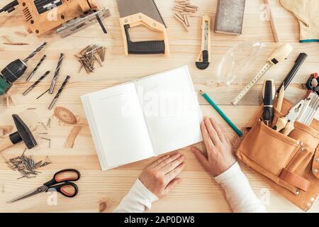 Female carpenter reading DIY project instruction manual in small business woodwork workshop, top view Stock Photo