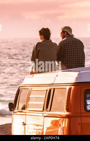 A couple sitting on top of their Volkswagen Campervan enjoying the evening light at Fistral in Newquay in Cornwall. Stock Photo