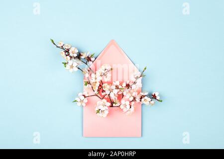 Pink envelope with branches of spring flower on blue background. Flat lay, top view. Minimal styled card.