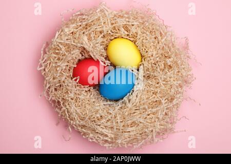 Nest with three easter eggs on a pink background. Close-up. Top view. Stock Photo