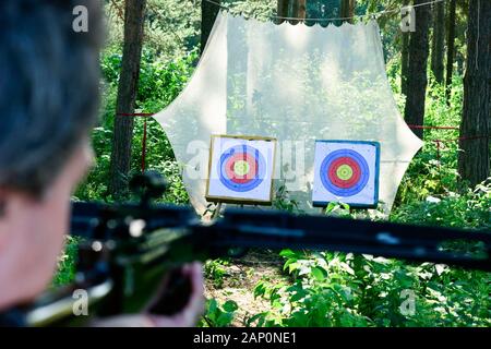 Man aiming crossbow at targets in summer forest Stock Photo