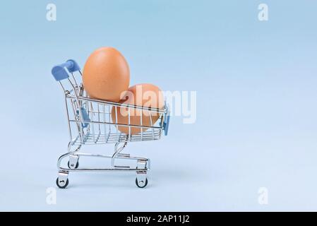 Shopping toy trolley with brown eggs on pastel blue background, minimal concept with copy space. Stock Photo