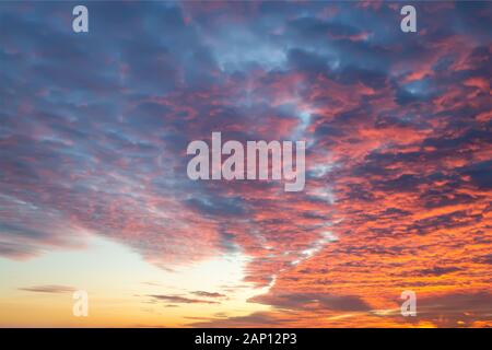 Sunset fire in the sky of natural color. Dark blue clouds with red reflections of the setting sun. Scenic cloudscape at sundown. Beauty in nature. Stock Photo