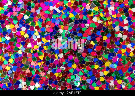 Background of heart shaped sparkles. Metallic scatter decorative texture. Multi colored foil confetti as backdrop for Valentine greeting card. Stock Photo