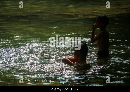 Two children are playing in the waterfall in a fun way. Stock Photo