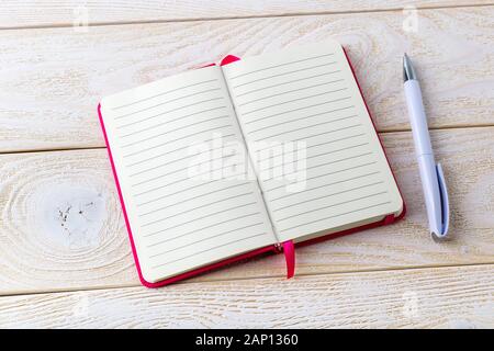 Opened lined paper notebook in a pink cover and white ballpoint pen on a white wood textured surface. Business, education and keep a diary concept. Stock Photo