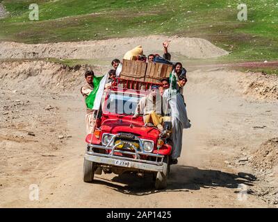 People are clinging to an overloaded jeep, driving on the dusty road up to Babusar Pass Stock Photo