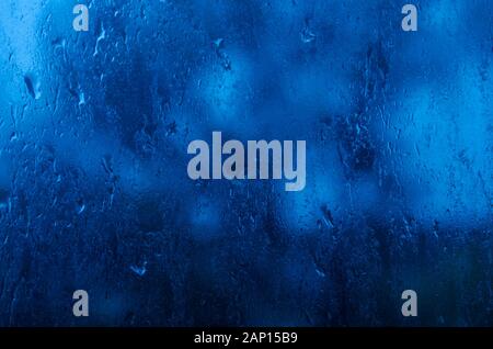 Raindrops on the window glass. Blue twilight light. Rainy weather. Stock Photo