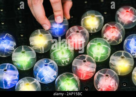 A man's hand inserts a lamp into an electrical panel. Colored light bulbs on a black panel. Radio electronic device Stock Photo