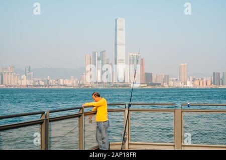 HongKong, China - November, 2019:  Fisher man with fishing rod on coast with HongKong skyline in background Stock Photo