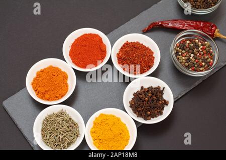Colorful various ground spices, saffron, caraway, curry, dry rosemary and cloves in porcelain and glass bowls on black stone cutting board with dry re Stock Photo