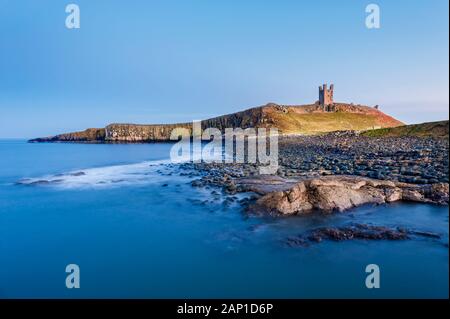 Dunstanburgh Castle and rocky and boulder covered  shoreline of Embleton Bay on the Northumberland coast Stock Photo