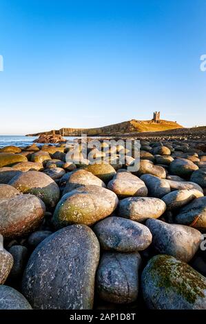 Dunstanburgh Castle and rocky and boulder covered  shoreline of Embleton Bay on the Northumberland coast Stock Photo