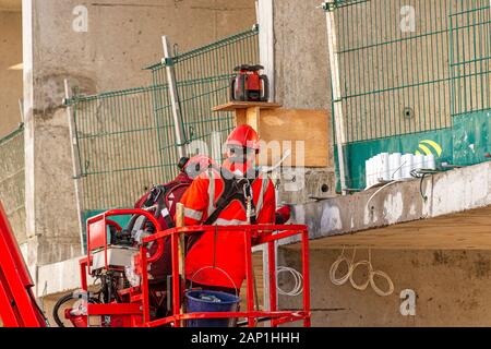 two male construction workers with red safety helmets on their heads and safety clothing perform an inspection on a concrete floor of a building under Stock Photo