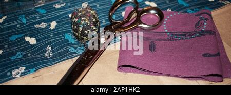 sisors and pincushion on top of cut, blue, Japanese cloth with fish and line pattern, and purple cloth with silk screen printing. Stock Photo