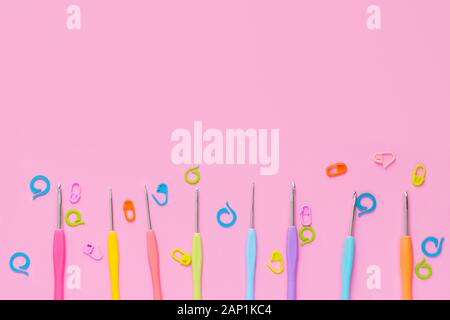 Different size crocheting hooks with colorful knitting accessories on pink background Stock Photo
