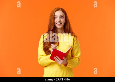 Inspired and upbeat, dreamy fascinated redhead girl writing down interesting lecture, smiling and gazing with admiration or enthusiasm, fill-in Stock Photo
