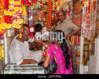 A vendor is selling artificial flowers and garlands in a colorful  shop Stock Photo